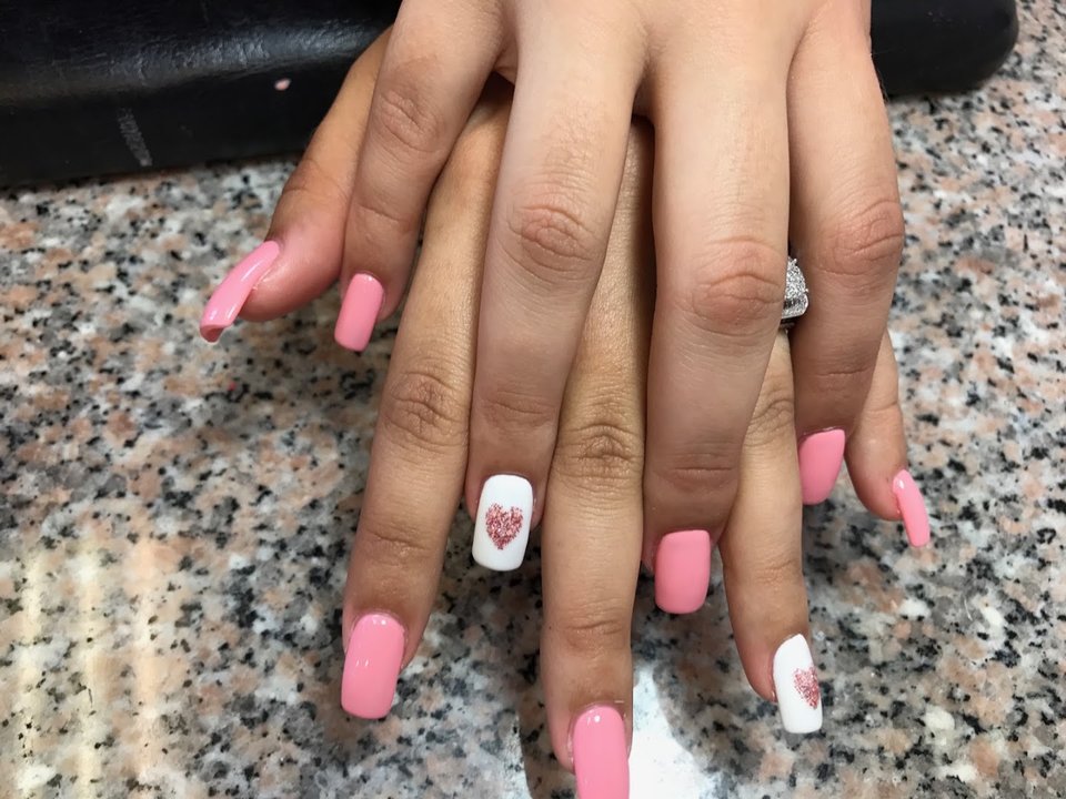 Nail technician shaping acrylic nails beside polish bottles.